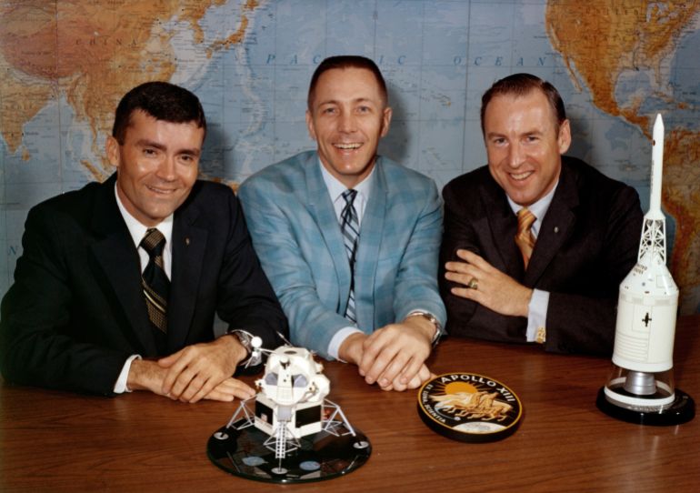 Red Haise, Jack Swigert e Jim Lovell posano su un tavolo di legno per una foto.