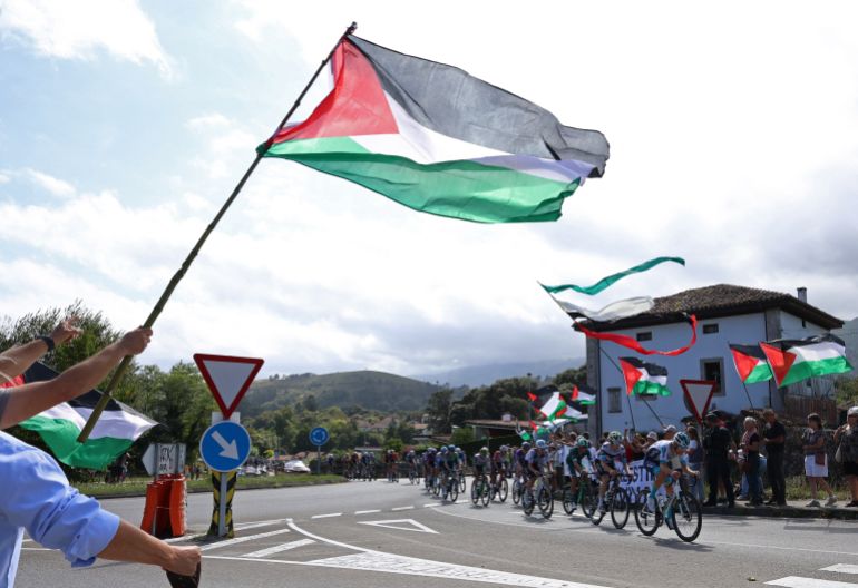 I cavalieri passano i manifestanti con bandiere della Palestina durante la fase 13 di Vuelta di Cycling A ESPANA