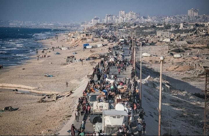 Una foto di persone in fuga su una strada costiera con la città di Gaza dietro di loro