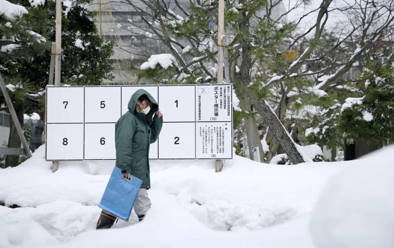 Una persona passa davanti a una bacheca con manifesti di candidati per le elezioni anticipate dell'8 febbraio, dove si è accumulata la neve, a Fukui, in Giappone, il 26 gennaio 2026, in questa foto scattata da Kyodo. Credito obbligatorio Kyodo/via REUTERS ATTENZIONE REDATTORI - QUESTA IMMAGINE È STATA FORNITA DA UNA TERZA PARTE. SOLO PER USO EDITORIALE. CREDITO OBBLIGATORIO. GIAPPONE FUORI. NESSUNA VENDITA COMMERCIALE O EDITORIALE IN GIAPPONE.