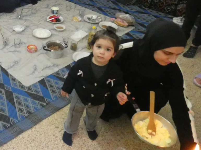 Una madre e una figlia condividono un pasto sul pavimento di un'aula.