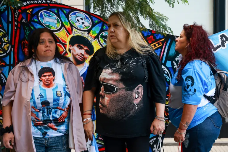 I tifosi della leggenda del calcio argentino Diego Maradona rimangono fuori da un tribunale durante l'udienza preliminare del processo sulla sua morte a San Isidro, periferia di Buenos Aires, il 14 aprile 2026. (Foto di Tomas CUESTA / AFP)