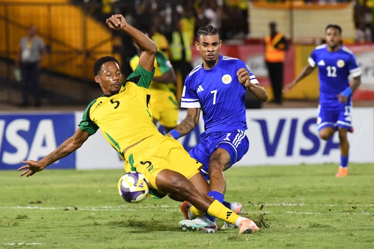 Juninho Bacuna di Curaçao, al centro, lotta per la palla contro Ethan Pinnock della Giamaica, a sinistra, durante una partita di calcio di qualificazione alla Coppa del Mondo 2026 a Kingston, Giamaica, martedì 18 novembre 2025. (AP Photo/Collin Reid)