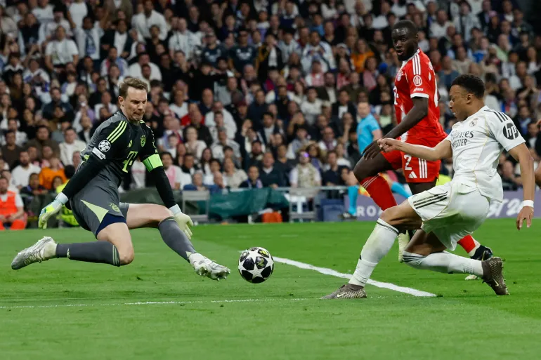 TOPSHOT - L'attaccante francese n. 10 del Real Madrid Kylian Mbappe (R) spara ma non riesce a segnare oltre il portiere tedesco n. 01 Manuel Neuer del Bayern Monaco durante la partita di calcio della prima tappa della finale dei quarti di UEFA Champions League tra il Real Madrid CF e l'FC Bayern Monaco allo stadio Santiago Bernabeu di Madrid il 7 aprile 2026.