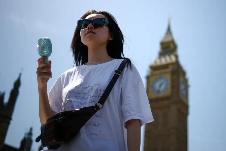 Una donna usa un ventilatore mentre cammina vicino al Parlamento, nel clima caldo di Londra, Gran Bretagna, 23 giugno 2026. REUTERS/Guglielmo Mangiapane IMMAGINI TPX DEL GIORNO
