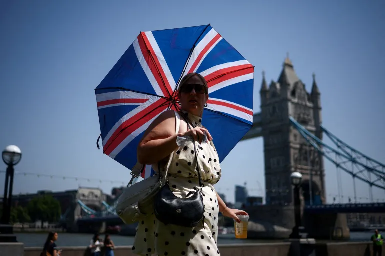 Una donna usa un ombrello per proteggersi dal sole mentre cammina vicino al Tower Bridge, in mezzo a un'ondata di caldo, mentre la Gran Bretagna sperimenta temperature record che interrompono le scuole e le reti di trasporto, a Londra, Gran Bretagna, 25 giugno 2026. REUTERS/Guglielmo Mangiapane IMMAGINI TPX DEL GIORNO