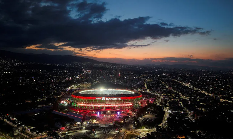 Lo Stadio Azteca si illumina al tramonto con una città buia alle spalle e nuvole in alto