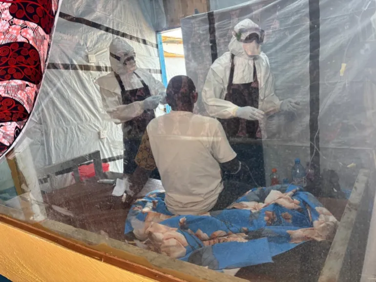 Operatori sanitari in tute protettive assistono un paziente in un reparto di isolamento presso il centro di trattamento di Rwampara, dove i medici affermano che il ceppo Bundibugyo può muoversi “silenziosamente” attraverso il corpo fino alle fasi finali.