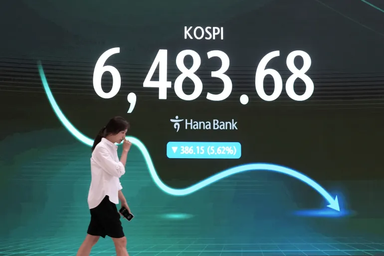 Un commerciante di valuta passa davanti a uno schermo che mostra il Korea Composite Stock Price Index (KOSPI) nella sala di negoziazione dei cambi della sede centrale della Hana Bank a Seul, Corea del Sud, mercoledì 19 agosto 2026