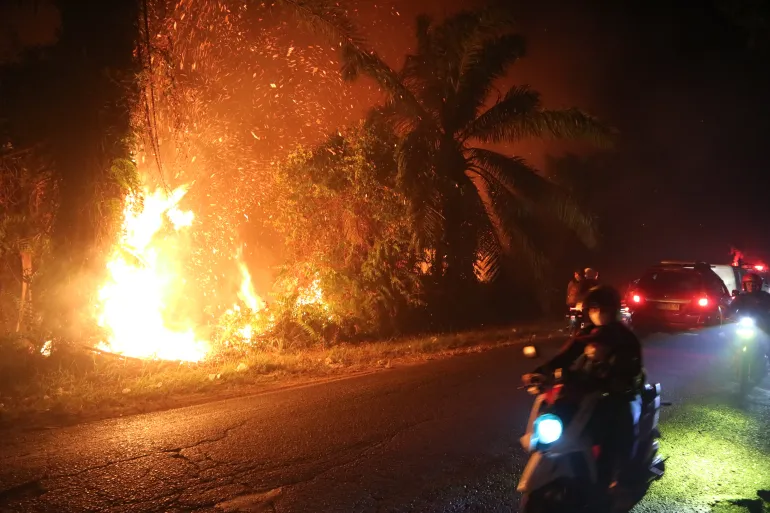 Gli automobilisti attraversano un incendio che brucia attraverso un campo di torbiere a Sampit, Kalimantan centrale, Indonesia, il 24 agosto 2026