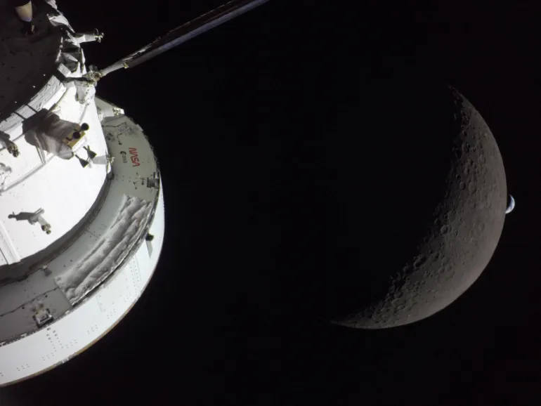 Una vista della navicella spaziale Orion della NASA in primo piano, illuminata dal sole mentre la Luna e la Terra sono visibili dietro di essa, come fotografato da una delle telecamere sui pannelli solari della navicella Orion durante il sorvolo della luna da parte dell'equipaggio di Artemis II il 6 aprile 2026