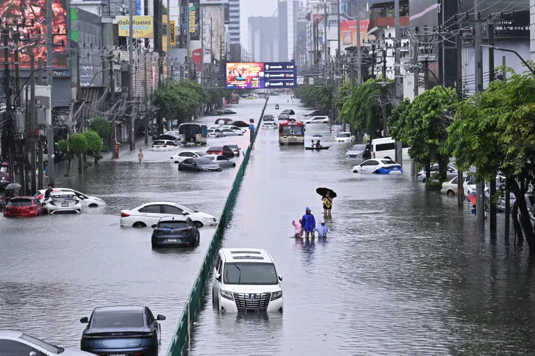 Persone passano accanto a veicoli abbandonati su una strada allagata di Petchaburi a Bangkok, il 26 settembre 2026.