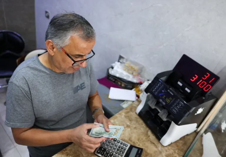 Un uomo conta le banconote in dollari americani in un negozio di cambio valuta a Baghdad, Iraq, 7 ottobre 2026 [Ahmed Saad/Reuters]