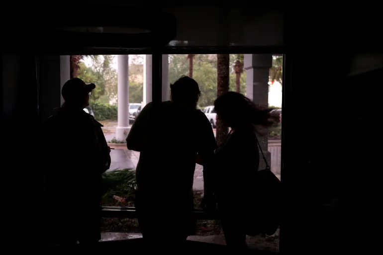 La gente guarda il vento, la pioggia e i detriti volanti dalla hall di un hotel durante un'interruzione di corrente prima dell'arrivo dell'uragano Isaias, a Pensacola, Florida, Stati Uniti, 9 ottobre 2026. REUTERS/Marco bello