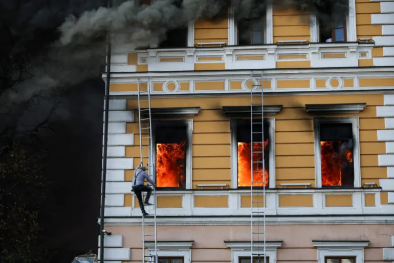 Ihor Malchevsky, 69 anni, vice capo dipartimento dell'Accademia nazionale delle scienze ucraina, usa una scala mentre le fiamme si alzano da un edificio amministrativo colpito da un attacco di droni a reazione russi, a Kiev, Ucraina, 28 settembre 2026