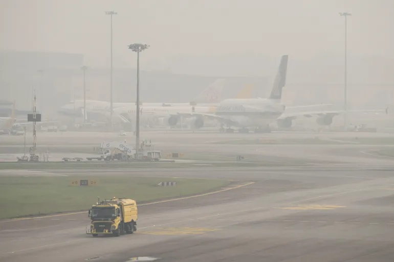 Un camion delle pulizie supera gli aerei parcheggiati sulla pista dell'aeroporto Changi di Singapore il 16 ottobre 2026, mentre il paese continua ad essere avvolto nella foschia causata dagli incendi in Indonesia [AFP]