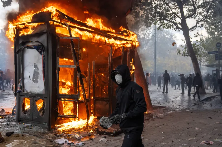 PARIGI, FRANCIA - 17 OTTOBRE: Un manifestante tiene in mano un sasso da lanciare alla polizia mentre un chiosco brucia durante una manifestazione vicino a Place de la République, mentre i Gilets Jaunes si uniscono agli studenti per un fine settimana di azione il 17 ottobre 2026 a Parigi, Francia. Il coinvolgimento dei Gilets Jaunes (Gilet Gialli) con i blocchi scolastici francesi in corso amplia la portata di queste manifestazioni collegando le lamentele studentesche localizzate a politiche economiche più ampie. I sindacati studenteschi hanno originariamente avviato il movimento per protestare contro il sottofinanziamento, il deterioramento delle infrastrutture e la grave carenza di insegnanti nelle scuole superiori e nelle università francesi. Unendosi alle proteste, i Gilets Jaunes introducono nell’azione guidata dai giovani la loro consolidata piattaforma contro i tagli di austerità, l’aumento del costo della vita e l’impennata dei prezzi del carburante. (Foto di Carl Court/Getty Images)